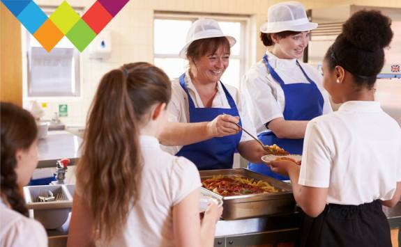 Two catering colleagues serve food to school children